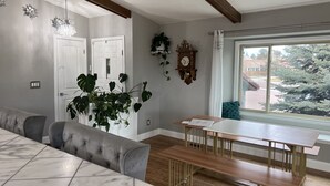 A dining area with a marble table, cushioned bench seating, a wooden bench, and a large window with a view of trees and buildings. - Hot Tub & Mountain Views; Theatre; Sauna; Piano; Two tier deck; Kid’s room (Colorado Springs)