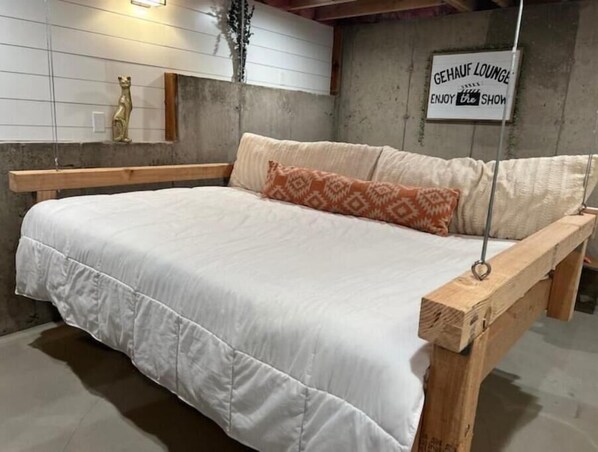 A bed with a wooden frame and white bedding, a small shelf with a golden statue, and a sign on the wall that reads "GEHAUF LOUNGE ENJOY the SHOW".