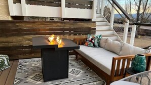 An outdoor seating area with a black table and a fire feature, a wooden bench, and a patterned rug. - Hot Tub & Mountain Views; Theatre; Sauna; Piano; Two tier deck; Kid’s room (Colorado Springs)