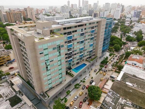 Un edificio de gran altura con varios pisos, una piscina en la azotea y un entorno urbano circundante.