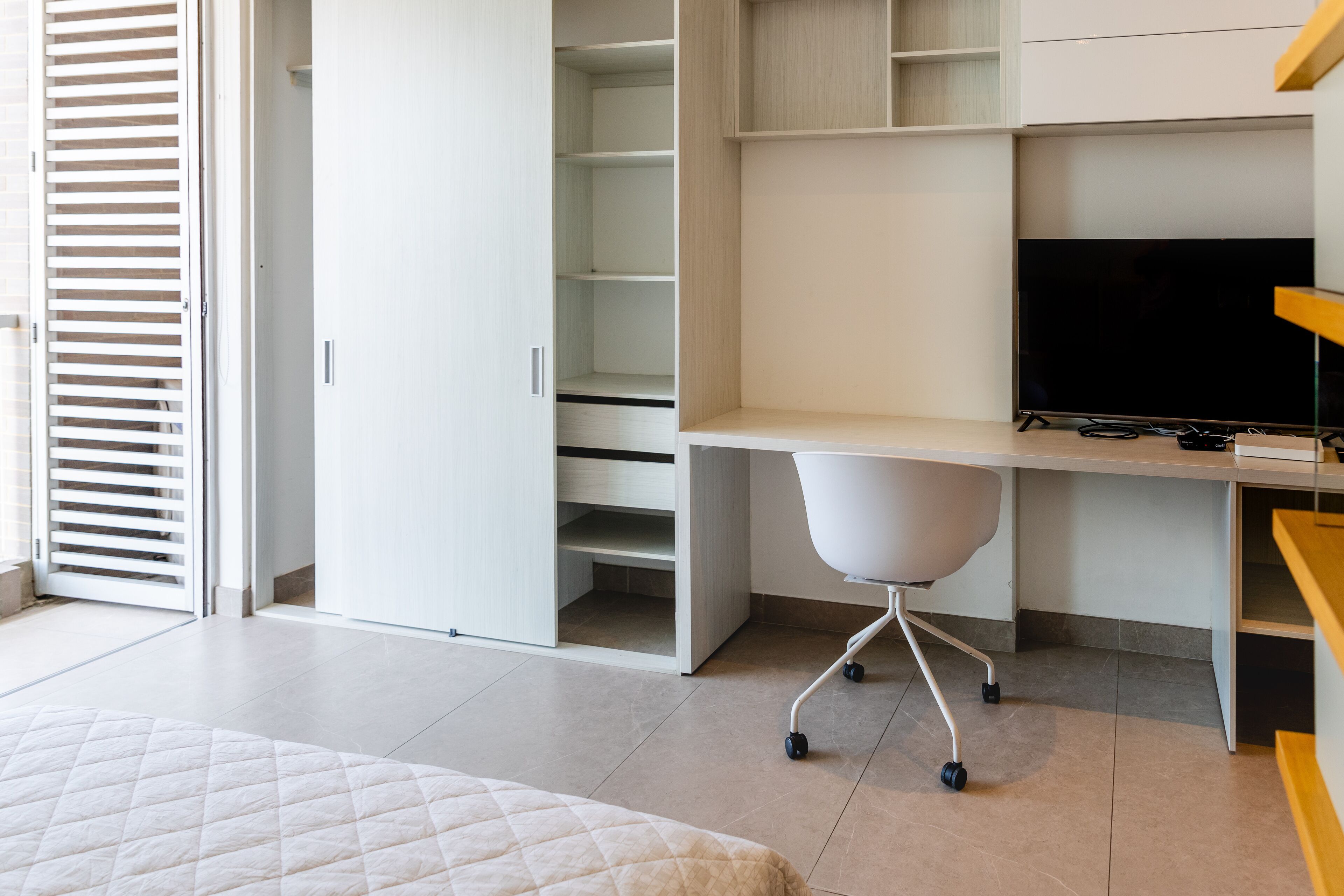Un dormitorio con cama, escritorio, silla, televisor y armario.