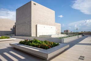 A modern building with a flat roof, large windows, and a flat facade. There are rectangular planters with green plants and red flowers in the foreground.