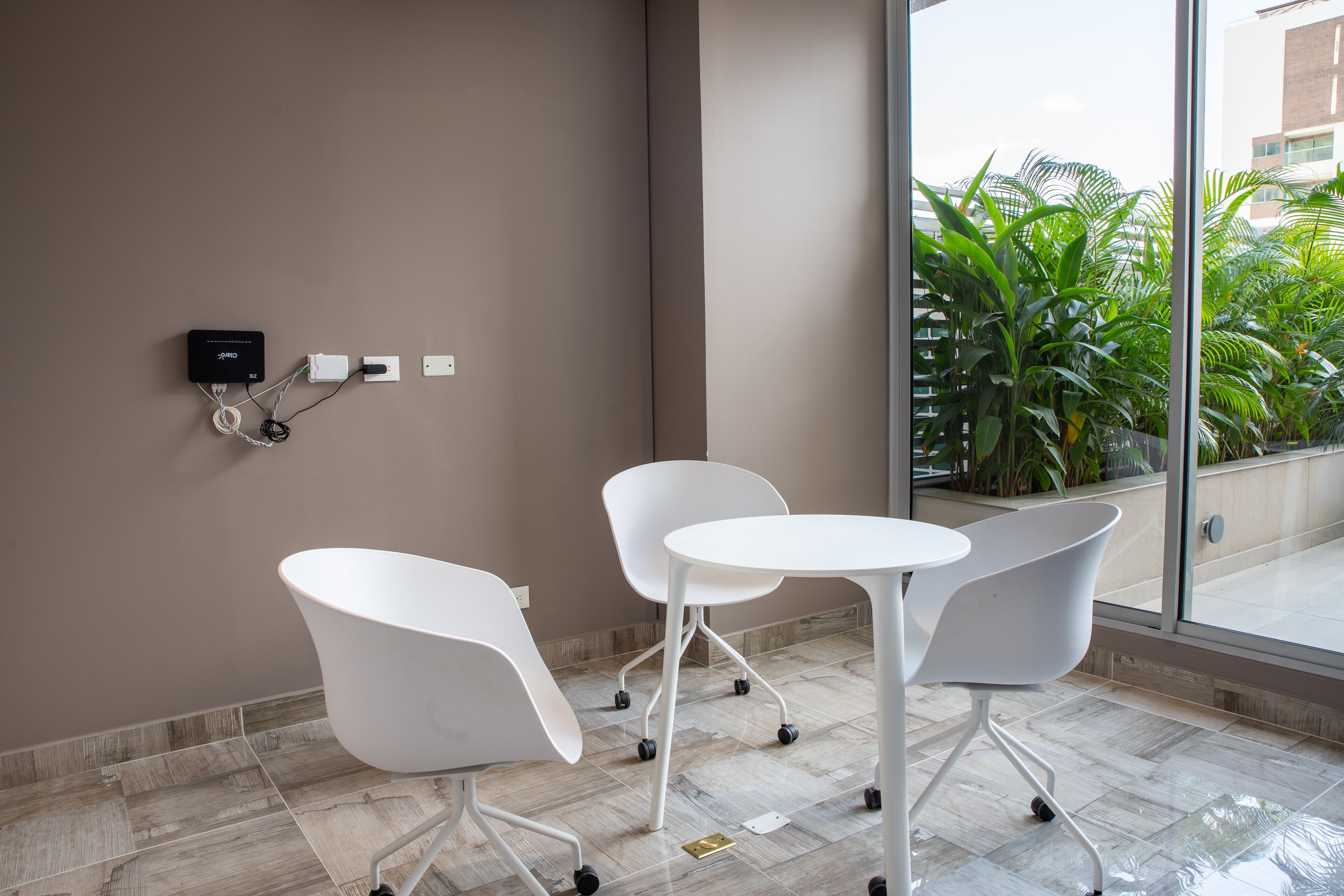 A modern room with a large window, white chairs, a small table, and a power outlet on the wall.