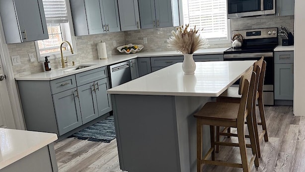 Een moderne keuken met grijze kastjes, een wit eiland en houten stoelen.