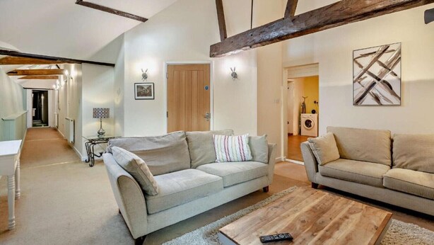 A spacious living room with two sofas, a wooden coffee table, and a ceiling with exposed beams. - 2 Bed Barn conversion (Tibenham)