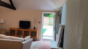 A living room with a television on a wooden cabinet, a sofa, and a door leading outside. - 2 Bed Barn conversion (Tibenham)