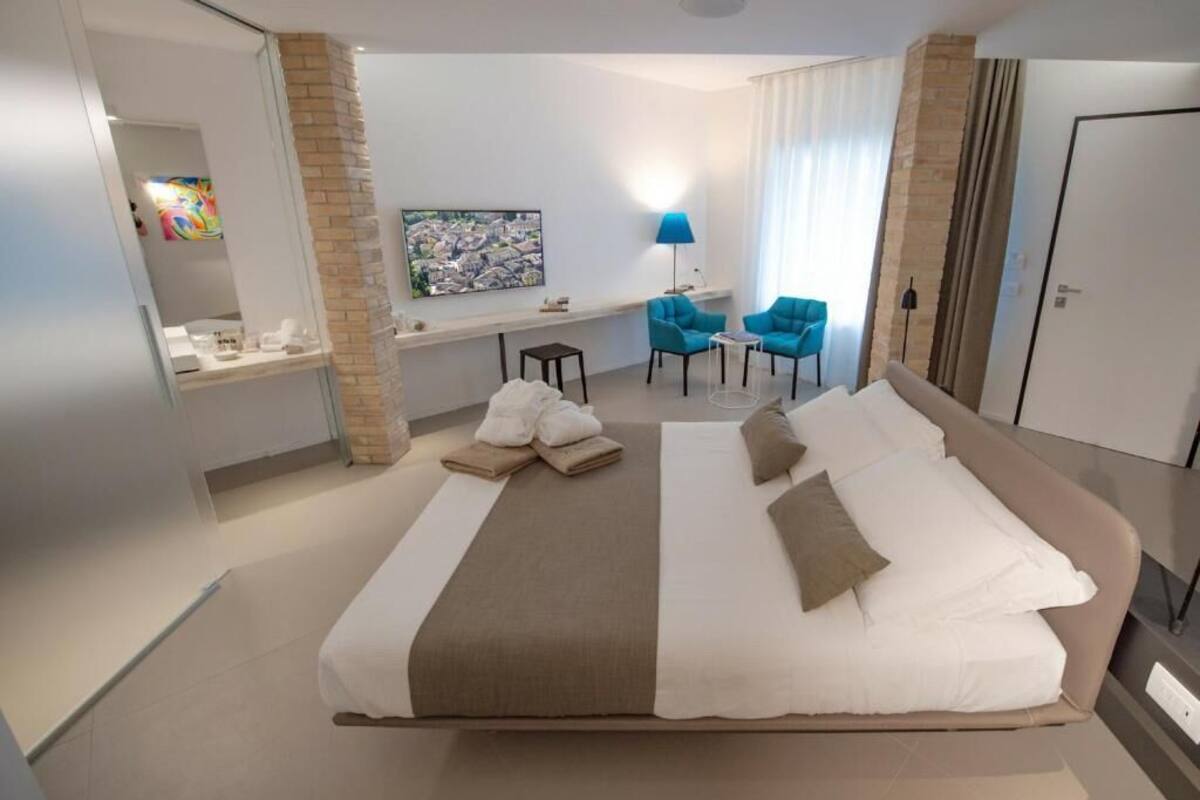 Une chambre d’hôtel avec un grand lit, un bureau avec une chaise, une petite table avec deux chaises, une lampe et un tableau au mur.