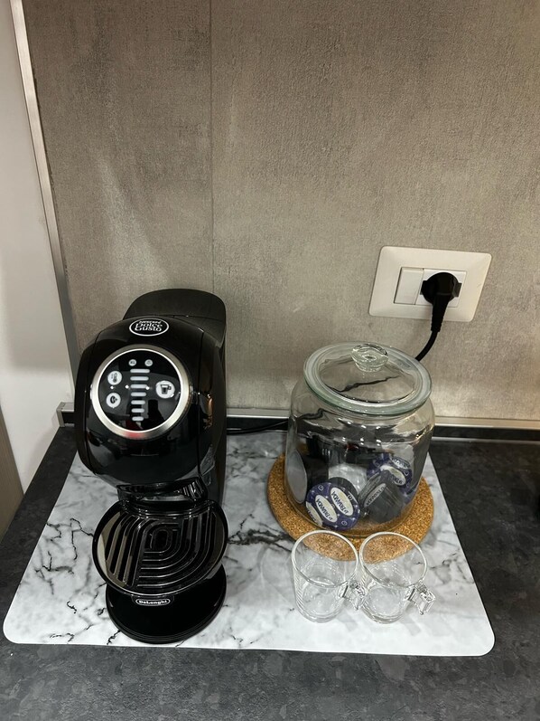 Eine Kaffeemaschine, ein Glasbehälter mit Korkenverschluss und zwei Gläser auf einer Marmorarbeitsplatte.