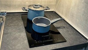 A compact kitchen with a built-in induction cooktop, a blue pot on it, and a smaller pot on a separate burner. - Gabry's House-Apartment equipped with all amenities in the center of Naples. (Napoli)