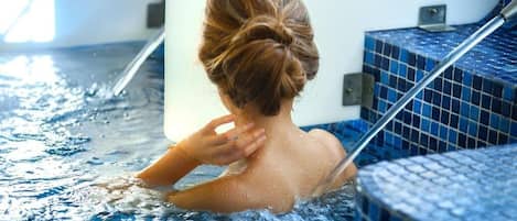 Una persona en un jacuzzi con pared de azulejos y una escalera metálica.