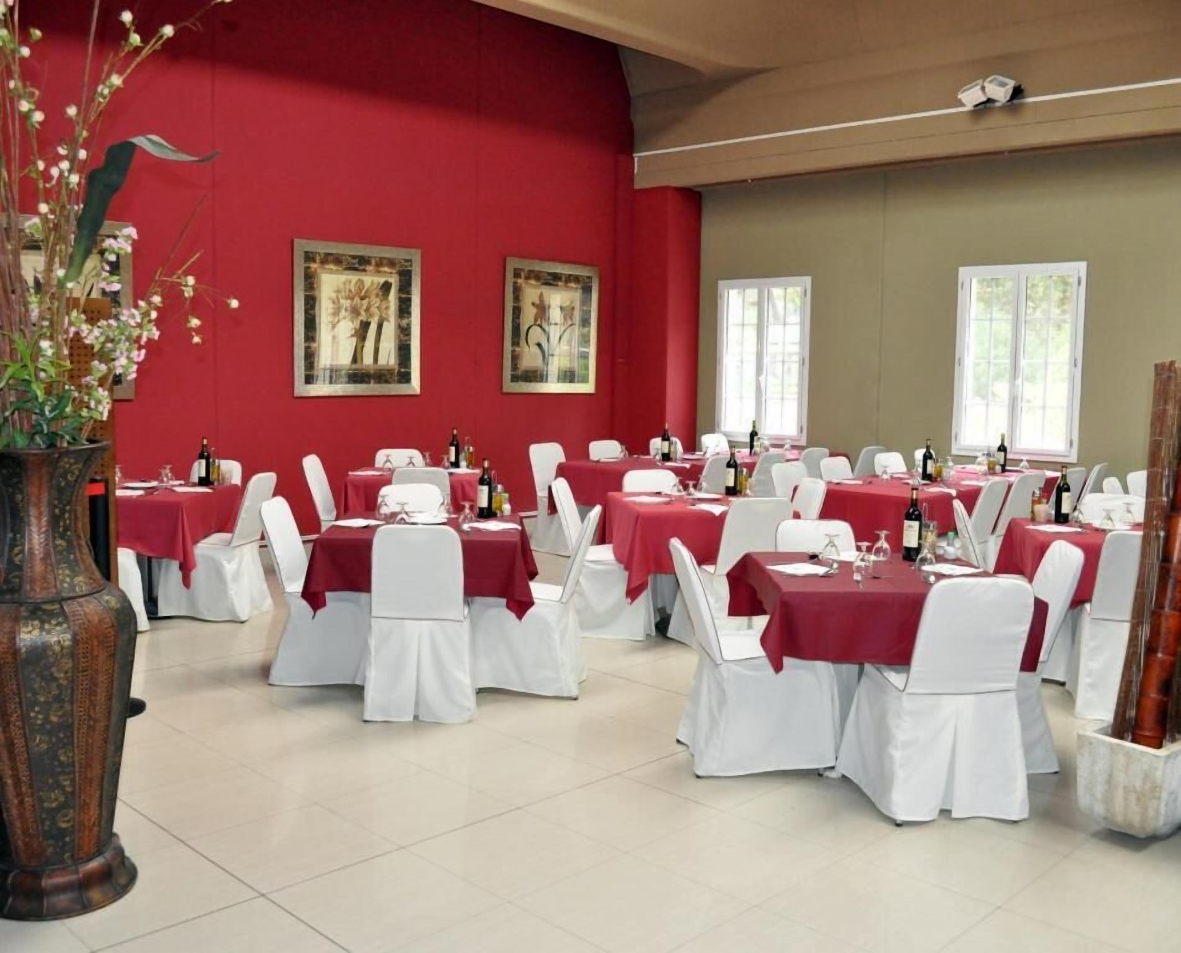 Een eetruimte met gedekte tafels voor een formeel evenement, met rode tafelkleden en witte stoelen.