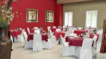 Een eetruimte met gedekte tafels voor een formeel evenement, met rode tafelkleden en witte stoelen.