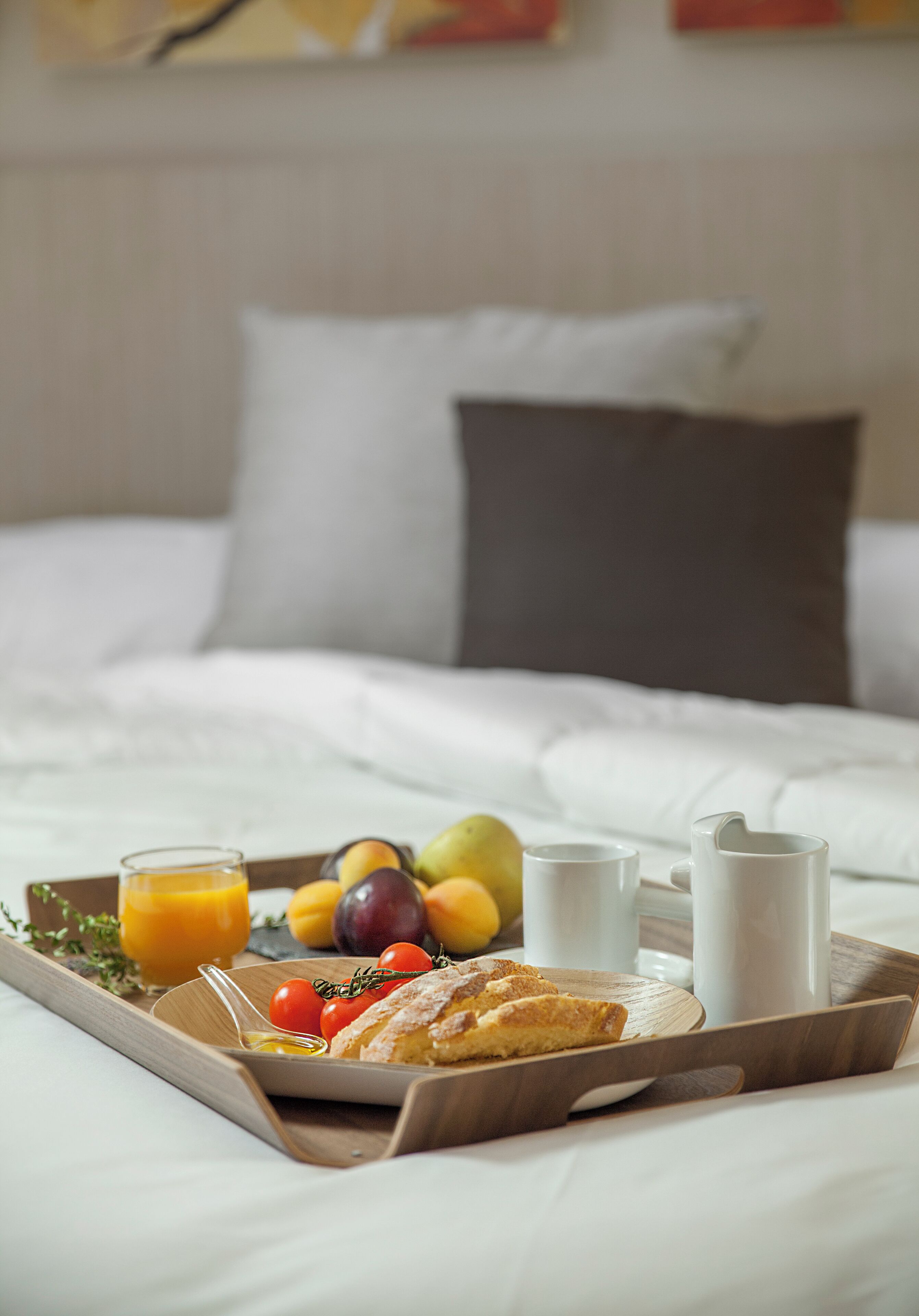 A breakfast tray with fruits, juice, and pastries on a bed with white bedding and a pillow.