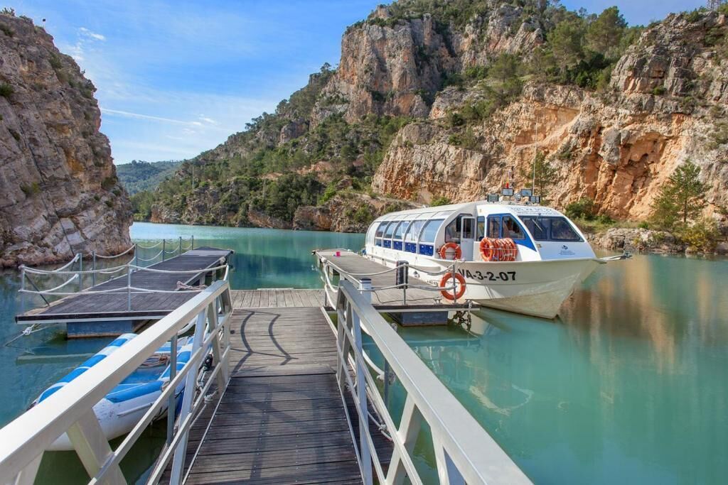 A boat docked at a pier with a rocky cliff backdrop.