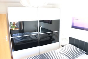 A modern bedroom with a bed, a wardrobe, and a TV mounted on the wall.