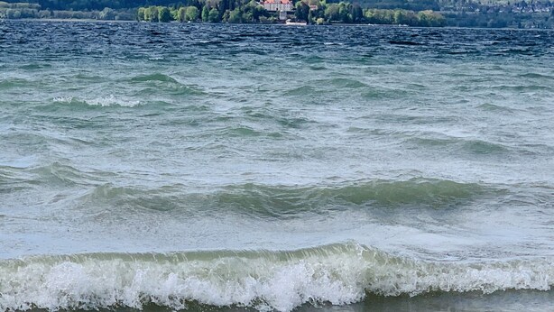 A lake with waves, a distant building, and a forested hill.