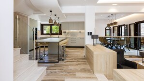 Una cucina moderna con isola centrale, sgabelli da bar e zona pranzo separata da un pannello di vetro.