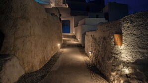 Un étroit sentier éclairé, bordé de murs de pierre, mène à un bâtiment doté d’une porte bleue.