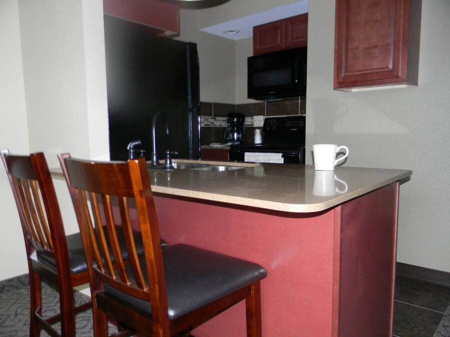 Una cocina pequeña con microondas, estufa y lavamanos. Hay dos sillas de madera y una taza blanca sobre la encimera.