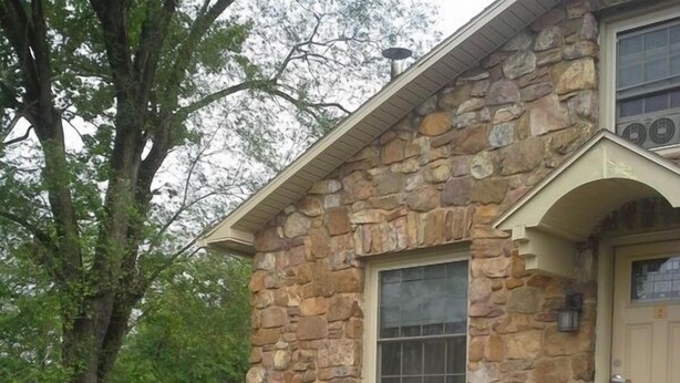Une maison en pierre avec un porche, deux chaises blanches et un escalier en briques.