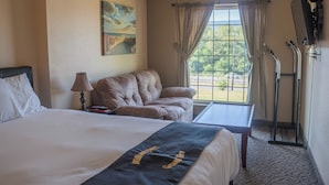 Une chambre d’hôtel avec un lit, un canapé, une fenêtre avec des rideaux, un tableau au mur et un téléviseur fixé au mur.