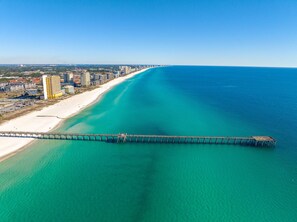 An aerial view of a coastal area with a long pier extending into the ocean, a sandy beach, and a row of high-rise buildings along the shore. - Sweet Coraline - 5BR/4BA, Private Pool, Steps to Beach Access, New Construction (Panama City)