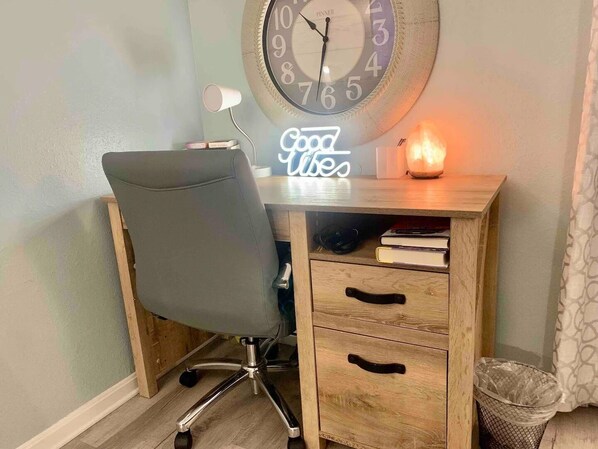 Een houten bureau met een stoel, een klok, een neonbord en een kaars.