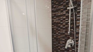 Een douche met glazen wanden, een betegelde muur, een handdouche en een kraan op de muur.
