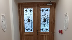 Een gang met twee houten deuren met decoratieve glaspanelen, een witte muur met een plaquette, en een betegelde vloer.
