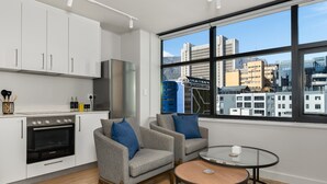 A modern kitchen with white cabinets, a built-in oven, and a large window offering a city view. - Stylish Minimalist: The Tokyo|Mountain and City View (Cape Town)