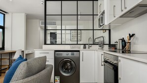 A compact kitchen with a built-in washer and dryer, white cabinetry, and a view through a large window. - Stylish Minimalist: The Tokyo|Mountain and City View (Cape Town)