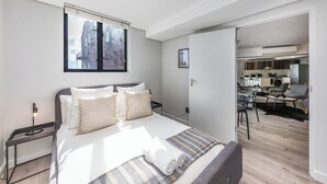 A modern hotel room with a large bed, a desk, and a view of the city through a window. - Modern Apartment in Trendy De Waterkant (Cape Town)
