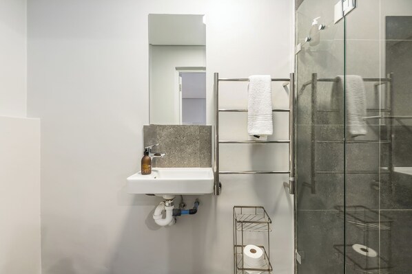 Un baño moderno con cabina de ducha de vidrio, un lavabo blanco con dispensador de jabón y un perchero para toallas.