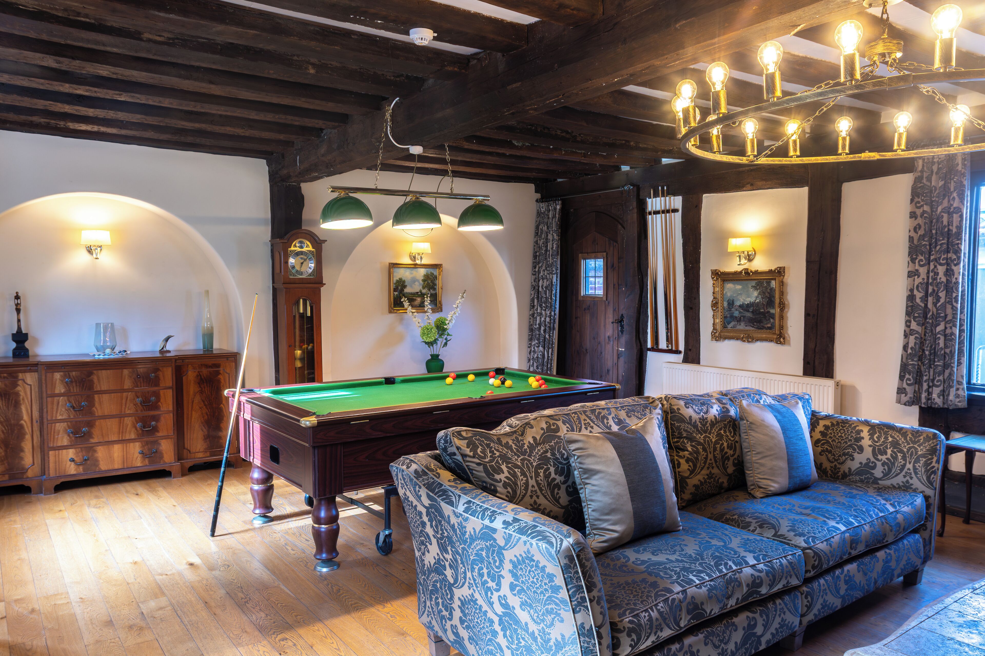 Une pièce avec une table de billard, un canapé, des meubles en bois et un lustre.