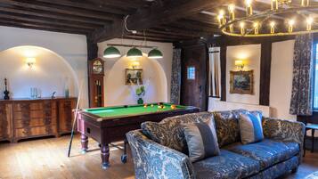 Une pièce avec une table de billard, un canapé, des meubles en bois et un lustre.