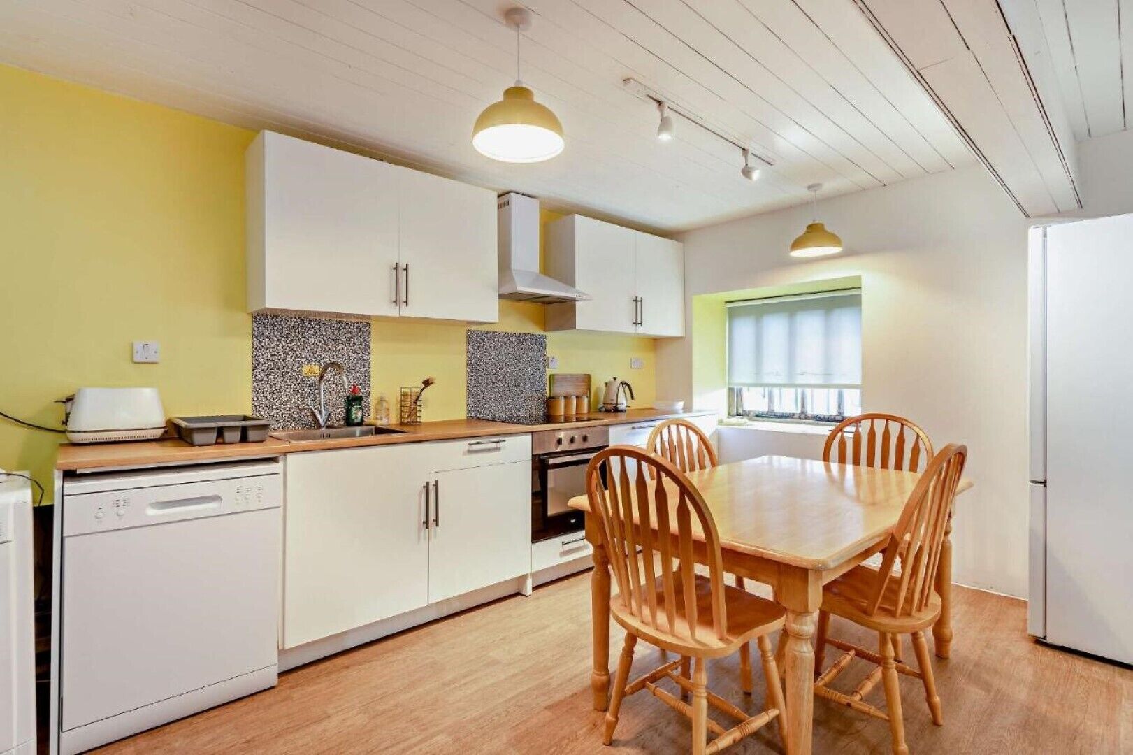 A compact kitchen with white cabinets, a wooden dining table, and four wooden chairs.