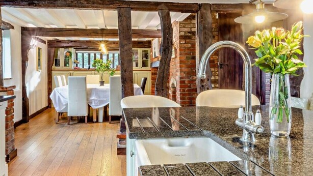 A modern kitchen with granite countertops, a stainless steel sink, and a dining area with a table and chairs. - Beautiful 10 Bed Oak beamed Country House (Tibenham)