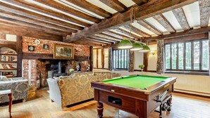 A room with a pool table, a sofa, a fireplace, and a large window. - Beautiful 10 Bed Oak beamed Country House (Tibenham)
