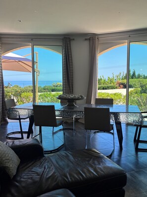 Ein Essbereich mit einem Glastisch und Stühlen, einem Ledersofa und Meerblick durch große Fenster.