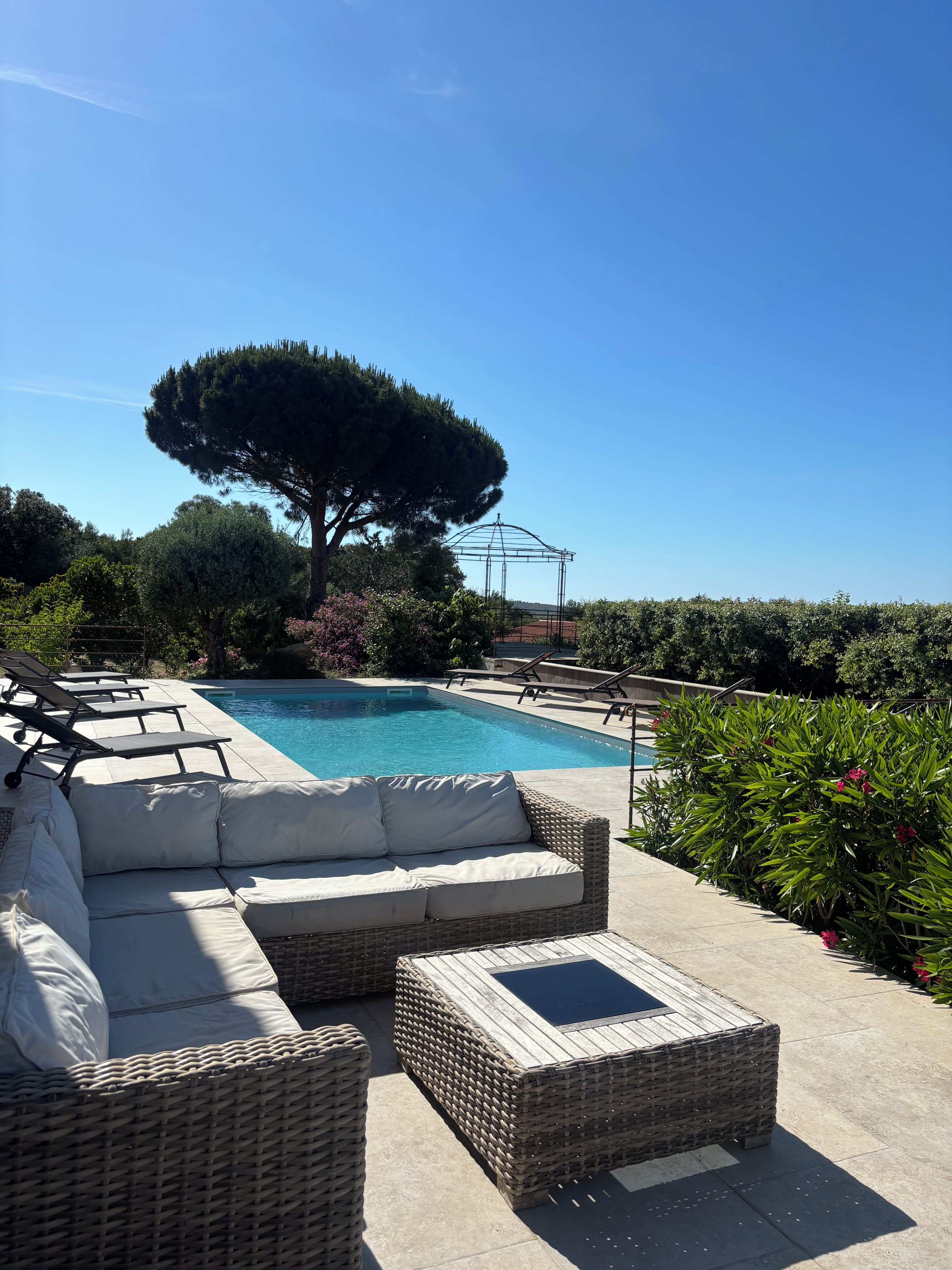 Un espace aménagé au bord de la piscine, avec des chaises longues, un canapé en osier et une pergola.