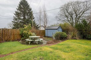 Ein Garten mit Holzzaun, einem blauen Gartenhaus und einem Picknicktisch.