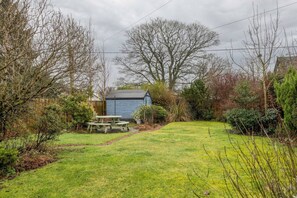 Ein Garten mit Holztisch und Bänken, umgeben von Bäumen und Sträuchern.