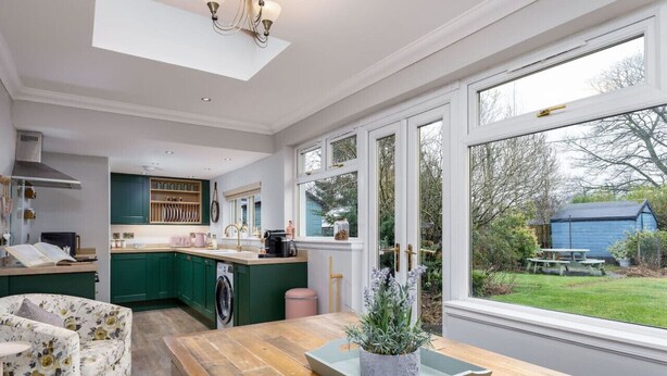 Una cocina moderna con un amplio ventanal, armarios verdes y una mesa de comedor de madera.