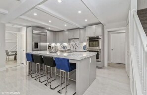 A modern kitchen with a central island, bar stools, stainless steel appliances, and a marble backsplash.