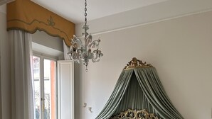 A bedroom with a four-poster bed, a chandelier, a radiator, and a view of the outside. - Charming residence inside a noble palace in the historic center (Rimini)