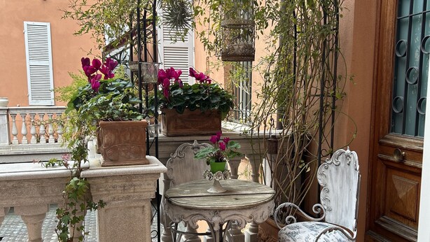 A small outdoor patio with a table and a chair, surrounded by potted plants and a wrought iron chair. - Charming residence inside a noble palace in the historic center (Rimini)