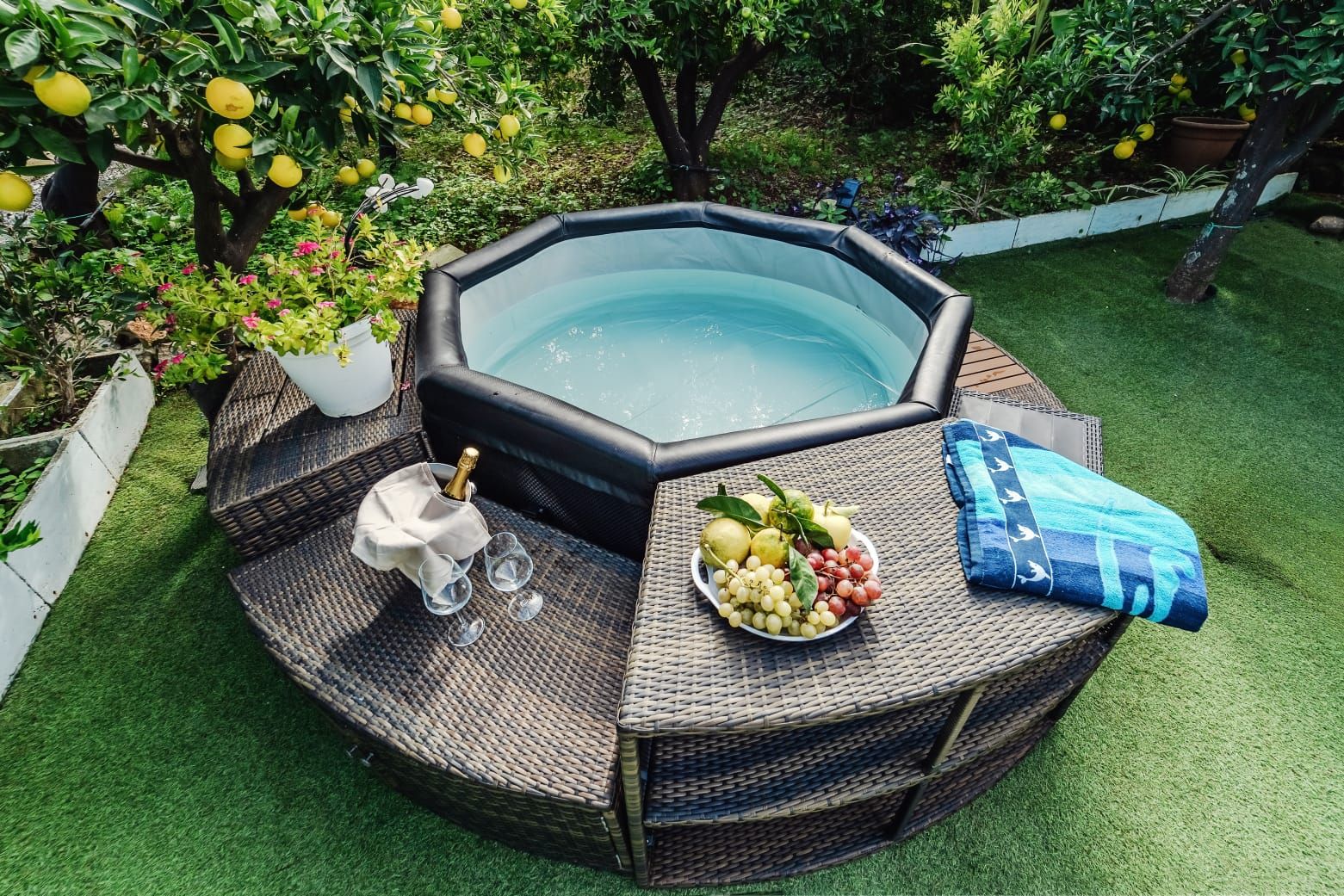 Un bain à remous entouré d’une table en osier, sur laquelle se trouvent un panier de fruits et une bouteille de champagne.