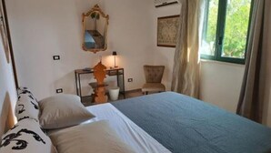 Ein Hotelzimmer mit Bett, Stuhl, Schreibtisch mit Lampe, Spiegel und einem Fenster mit Vorhängen.