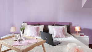 Un dormitorio con cama, una laptop, un florero con una flor, una bandeja con una taza y dos lámparas de noche.