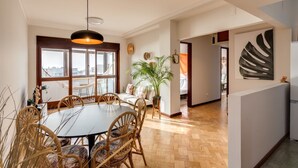 Een ruime woonkamer met een eettafel, stoelen, een groot raam en uitzicht op de stad.